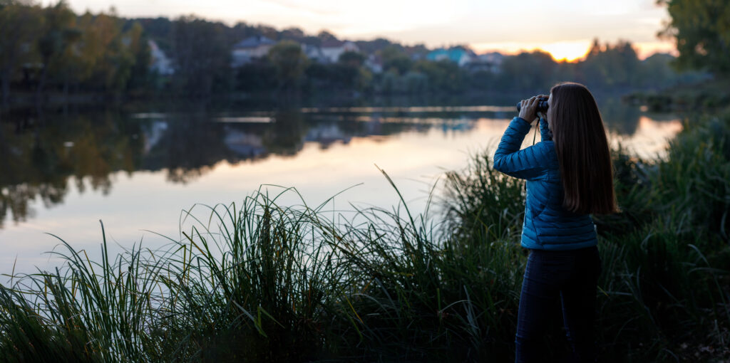 woman with binoculars bird watching at a New England lake