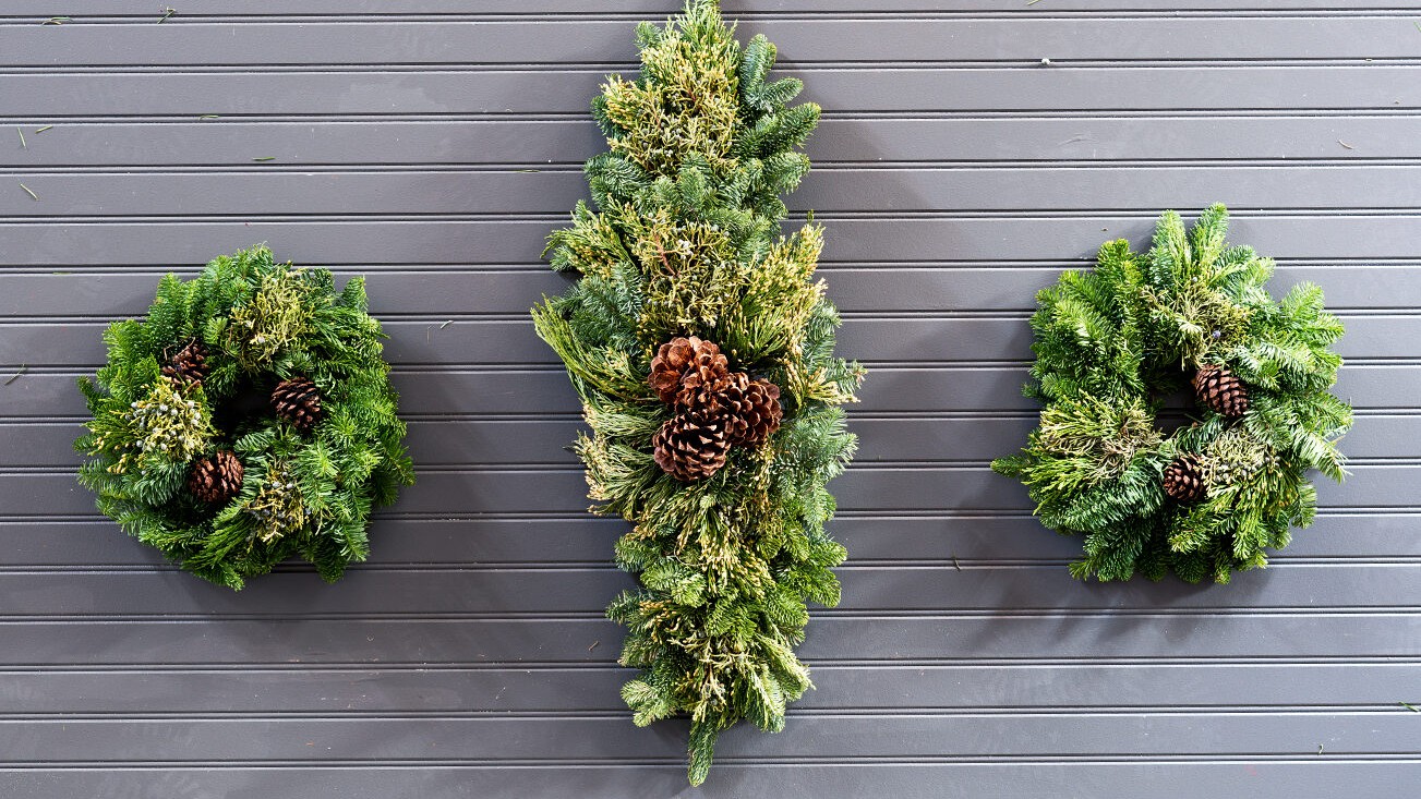 Two handcrafted wreaths and a fresh evergreen centerpiece decorated with pine cones and mixed greens for the holidays.