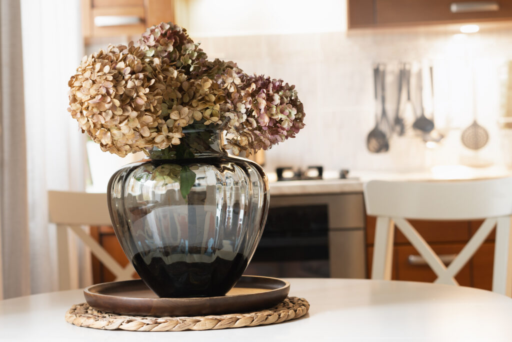 Dried hydrangea flowers in soft pink and tan tones arranged in a glass vase on a table.